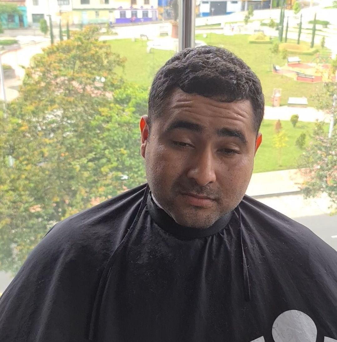 Foto de un integrante con capa de peluquería mirando resignado.